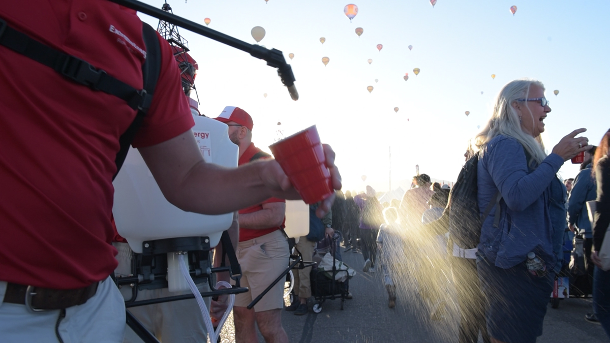 A man dressed as a corporate spokesman sprays mysterious liquid into a red cup with a pesticide sprayer, part of The Yes Men's action against ExxonMobil at Albuquerque Balloon Fiesta.