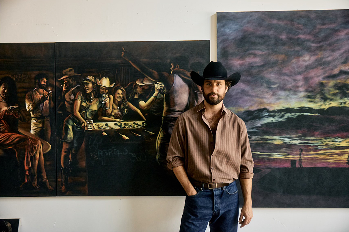 Image of artist RF. Alvarez in his studio in front of two paintings