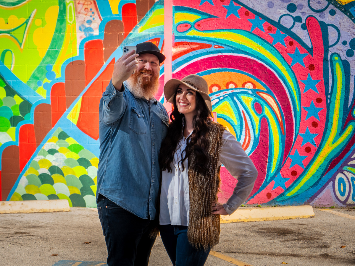 A couple posing for a selfie in front of a colorful abstract mural by Mario Enrique Figueroa, Jr in Houston.