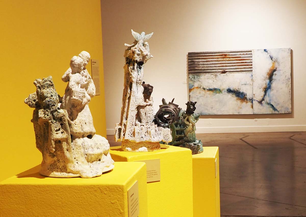 Installation view of Shifting Topographies, with ceramic figures by Jeff Schmuki in the foreground and abstract painting by Carol Hartman in the background.