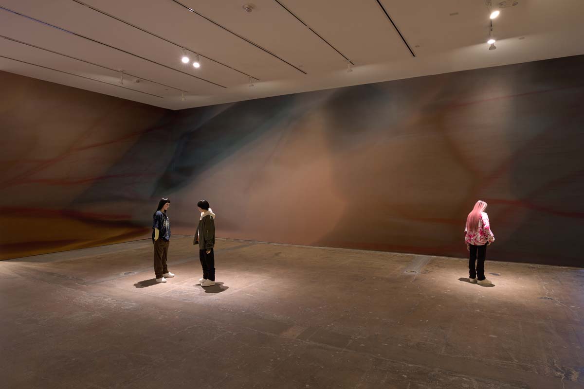 Installation view with three life-size doll figures in front of a photo mural.
