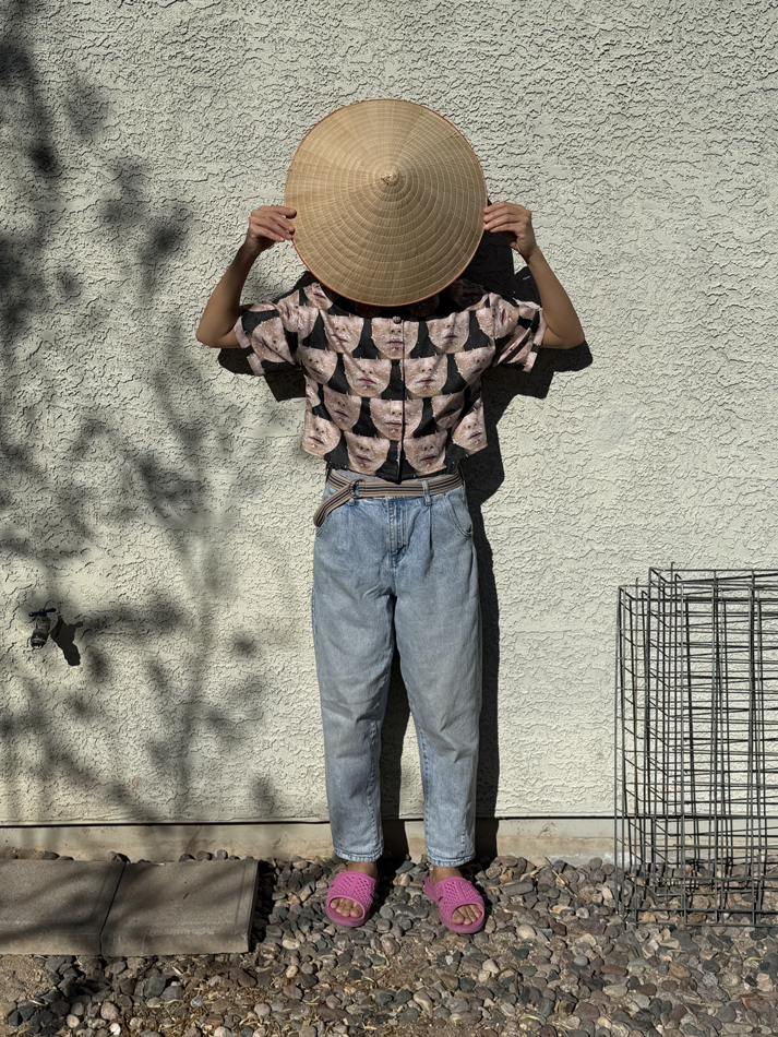 Portrait of artist Anh-Thuy Nguyen holding a Vietnamese hat in front of her face.