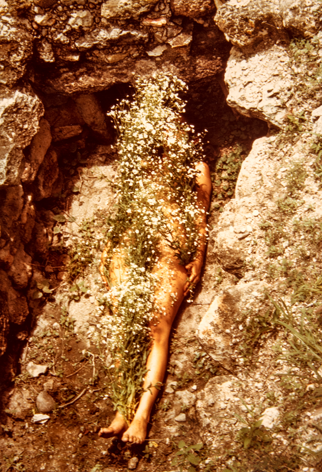 Ana Mendieta lies in a rocky landscape covered with flowers in her work Yaagul, featured in the Lucy Lippard exhibition.