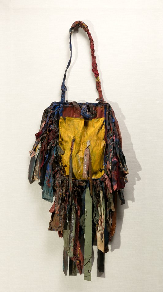 A hanging bag made from painted cloth and fabric strips appears in Harmony Hammond’s sculpture Bag IX, featured in the Lucy Lippard exhibition.