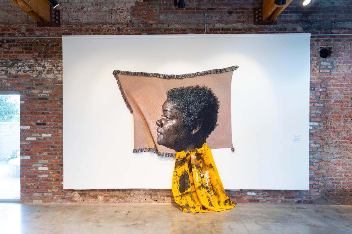 Johannes Barfield, The Green House on Cornell BLVD, a photograph printed on woven fabric, yellow canvas, asphalt, hand-harvested red clay soil 