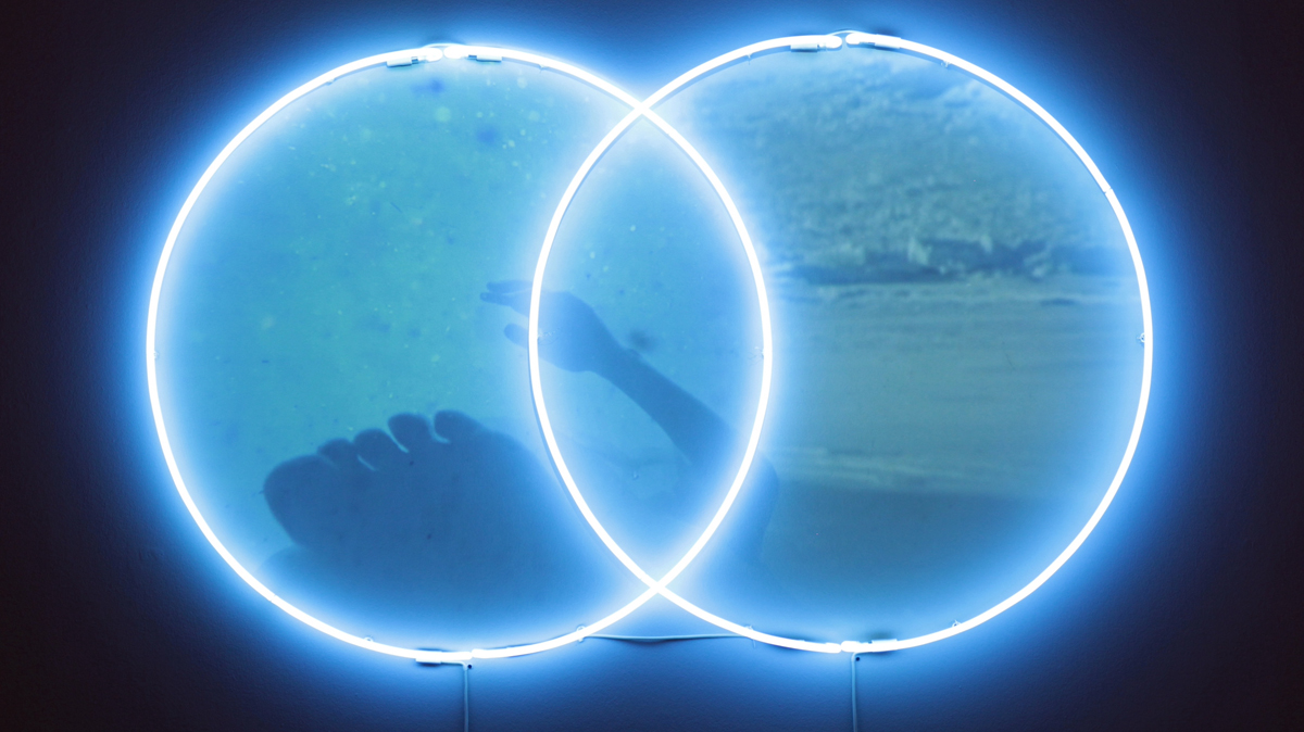 Neon artwork by Lily Reeves and Krista Davis featuring two overlapping blue circles and a projected image.