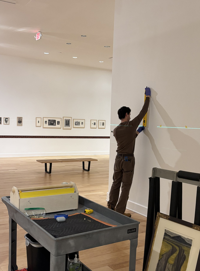 A preparator at El Paso Museum of Art installs artwork using a laser level.