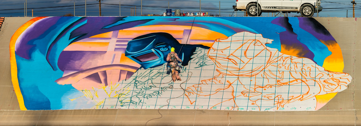 A muralist works semi-vertically on a massive mural in Pueblo, Colorado.