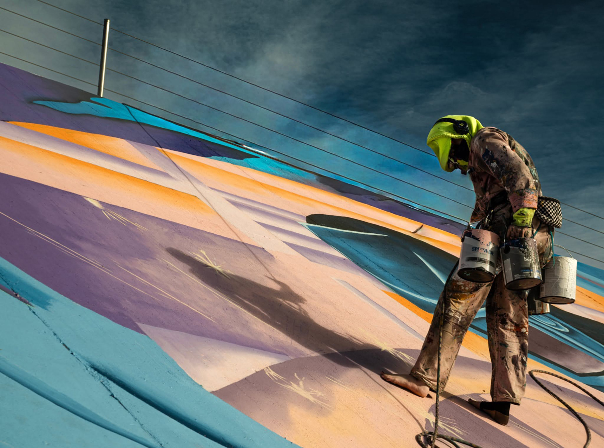 An artist rappels down a levee in Pueblo, Colorado, to add to the Pueblo Levee Mural Project.