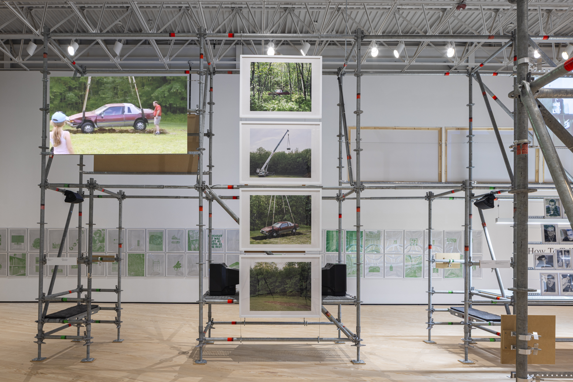 Installation view with photographs of a car mounted on scaffolding