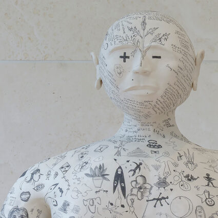 Installation view of a figurative sculpture covered in surreal marks.