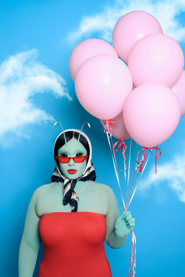 Faye Lenore, aka Ahubo the Alien, wearing a stylish scarf and holding pink balloons.
