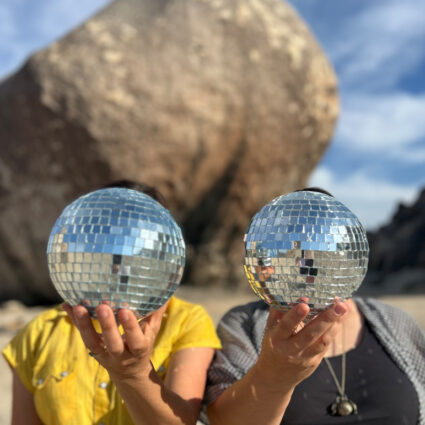 Two people holding up disco balls in front of their heads.