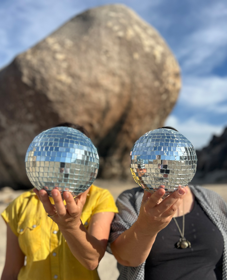 Two people holding up disco balls in front of their heads.