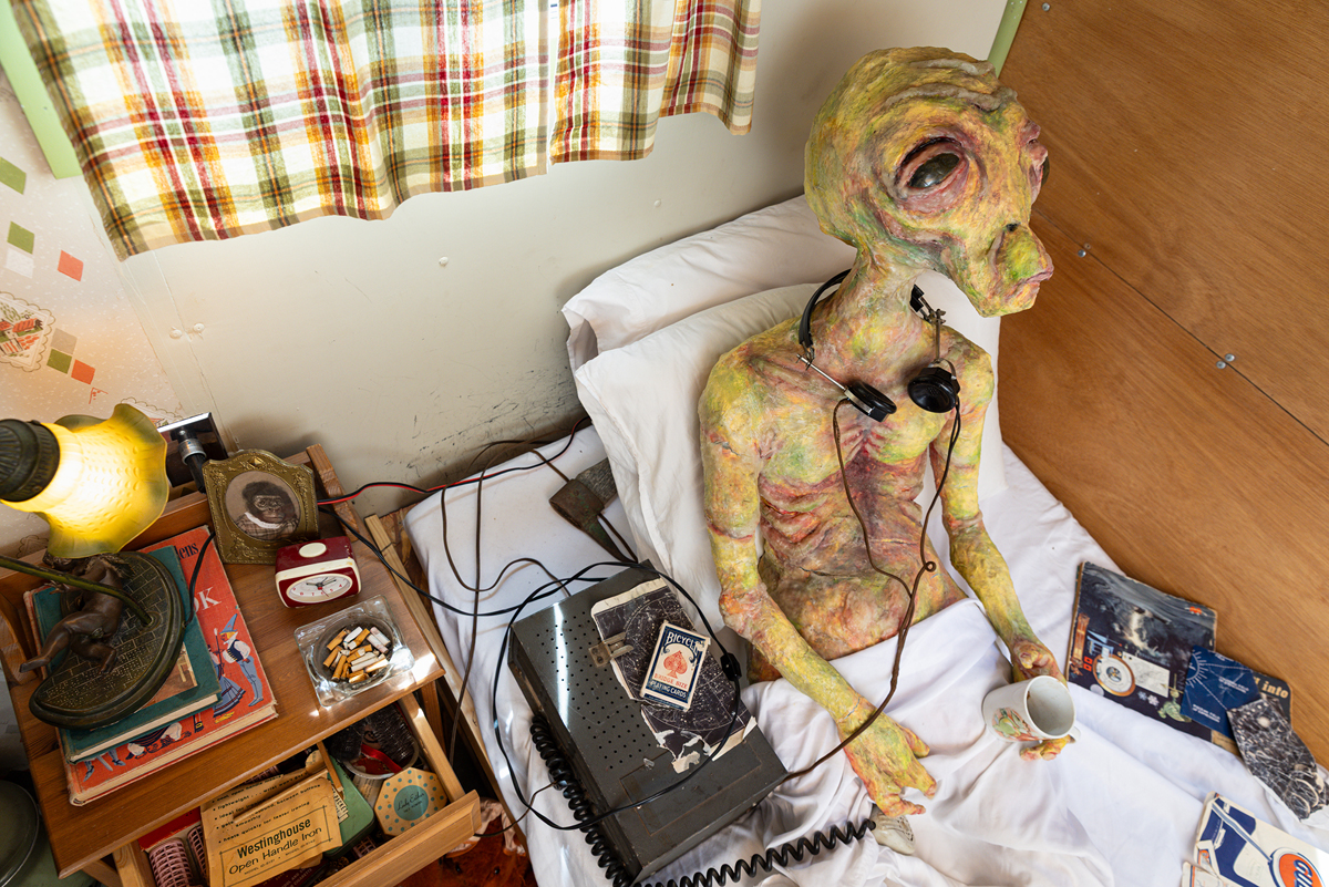Alien statue listening to music in a bed