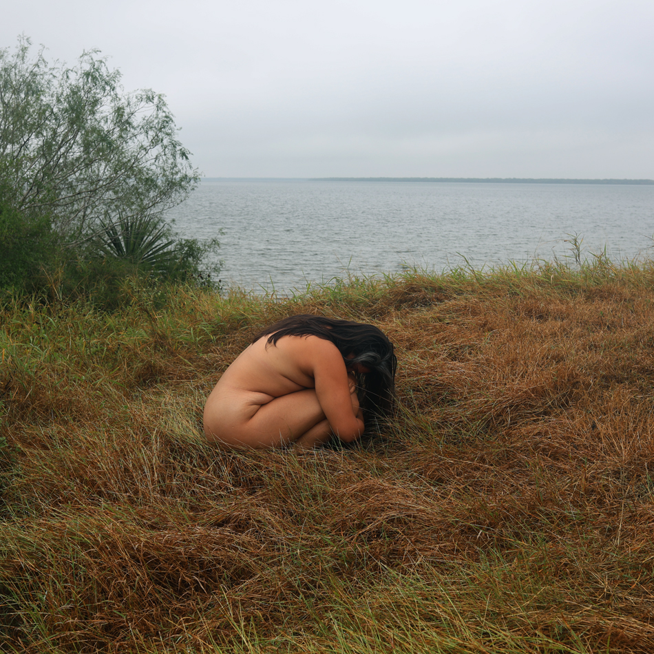 Photograph of person huddled naked in a field