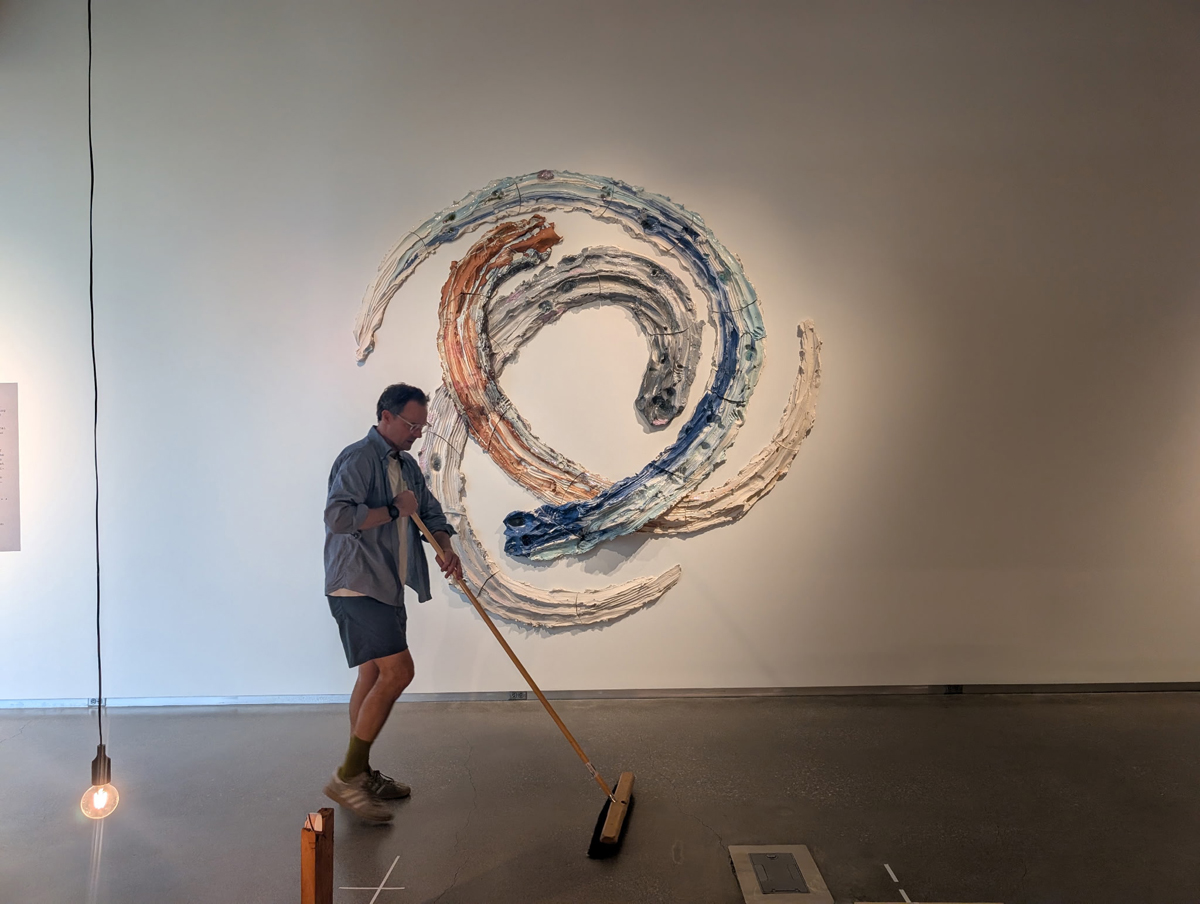 A museum worker sweeps in front of a wall sculpture by Brie Ruais.
