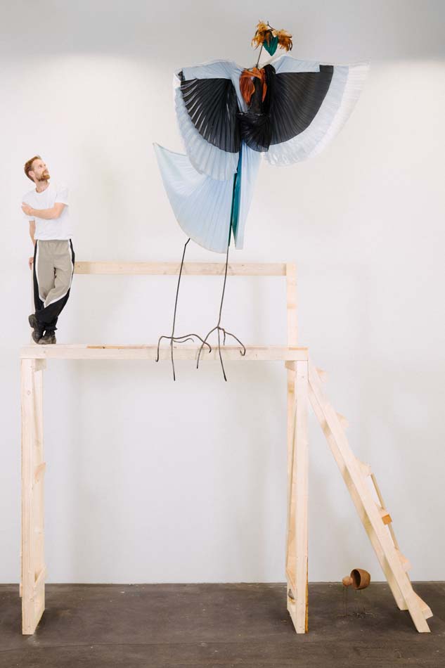 Photo of artist Petrit Halilaj, winner of the 2027 Nasher prize, standing atop a wooden fram structure with an abstract sculpture of a bird nearly double his height. Halilaj's win is one top Southwest Art News November 2025 headline.